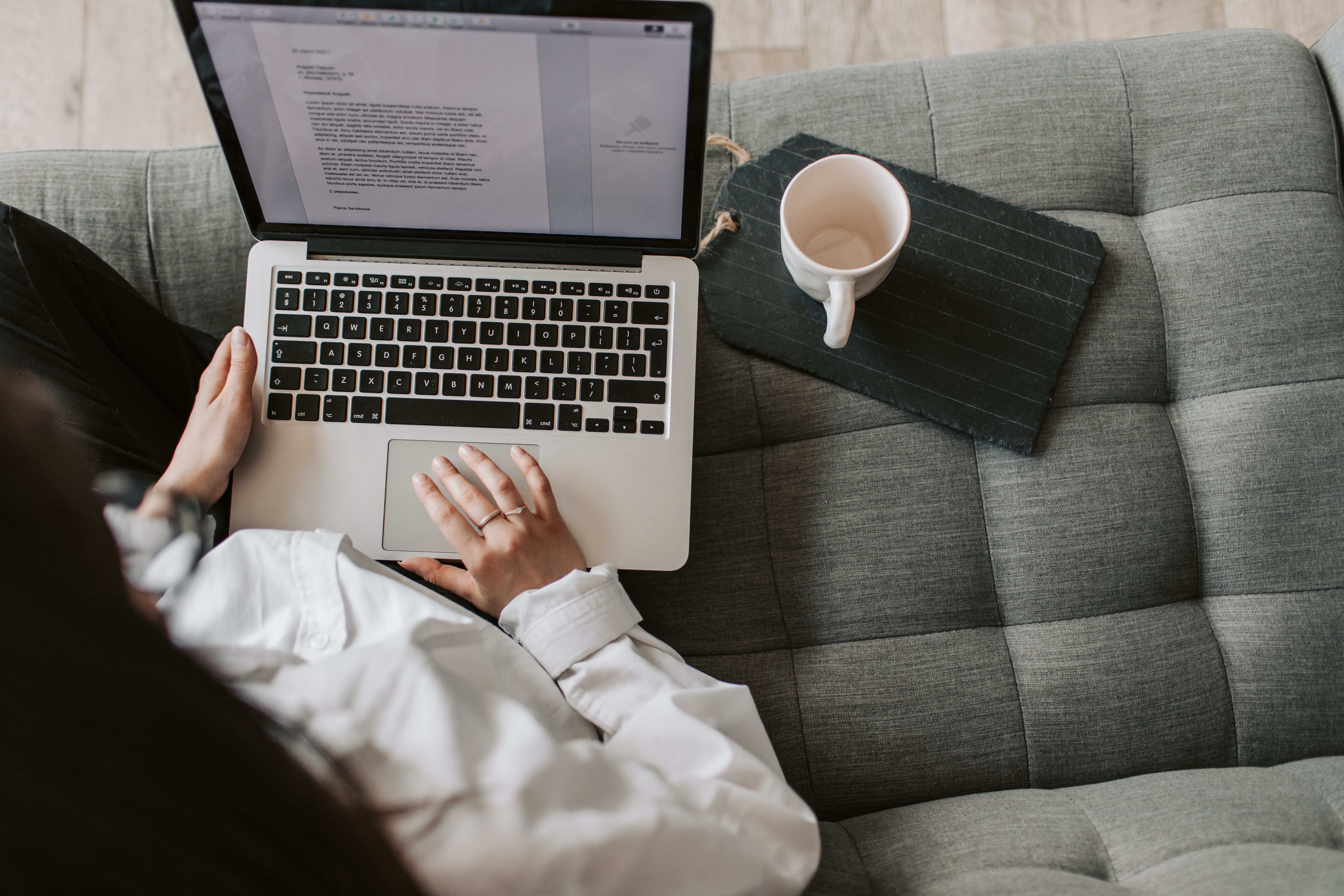 woman writing a letter on a laptop while sitting on a couch next to an empty cup of coffee